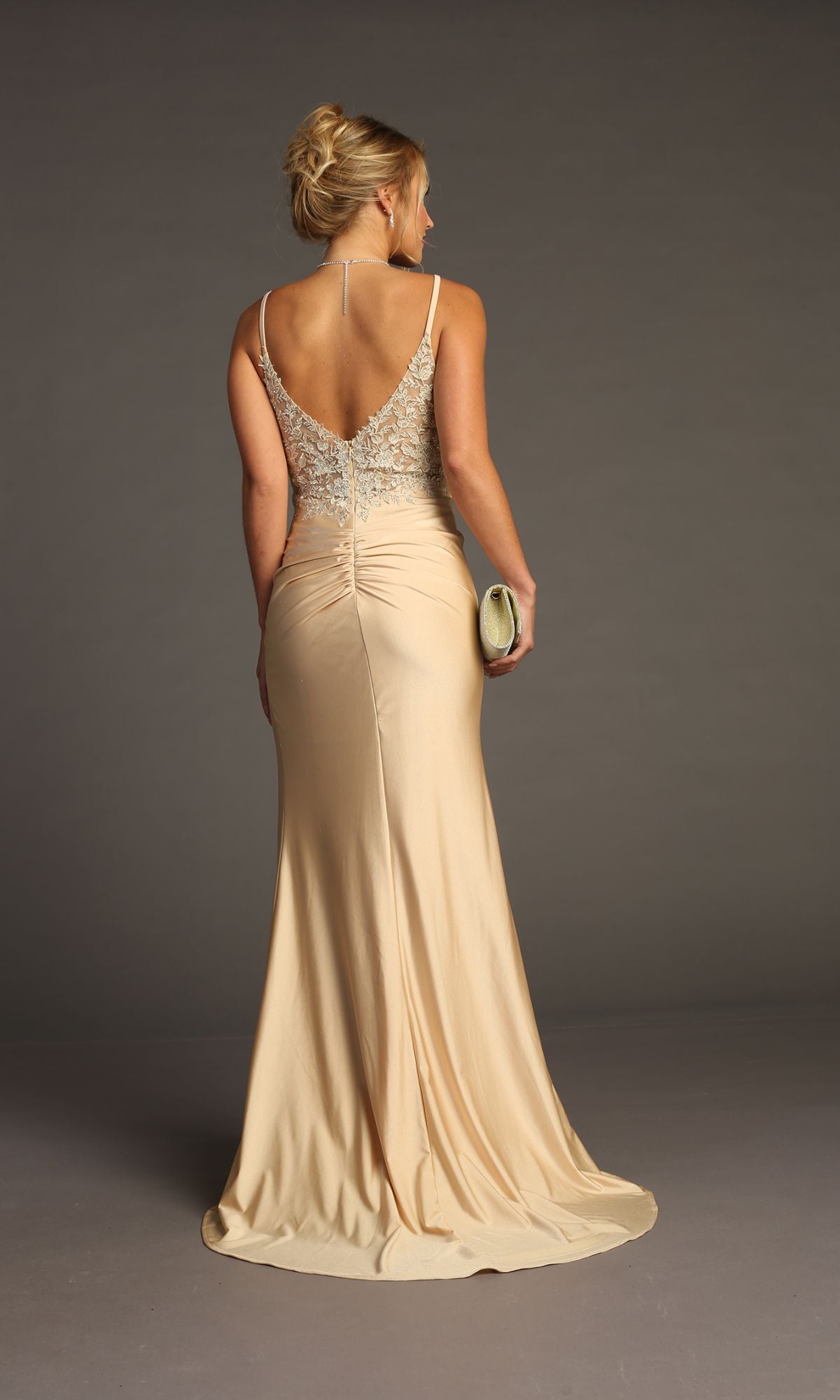 A woman in a floor-length, champagne-hued Lace-Bodice Slinky Long Prom Dress (Chicas YG5033) holds a clutch with her back to the camera, standing against a plain background.